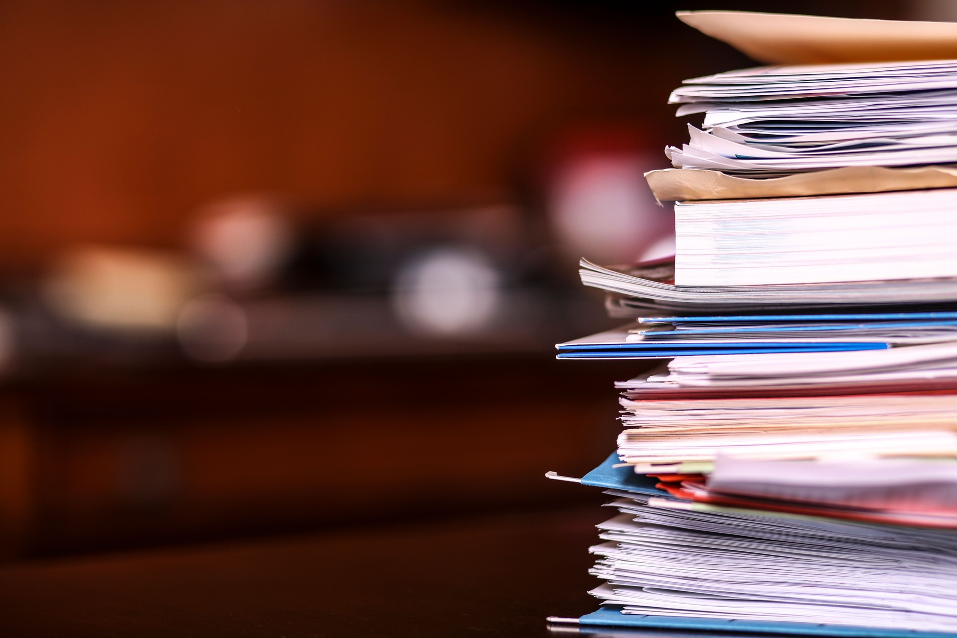 Business: Large stack of file folders, bills, paperwork on office desk.